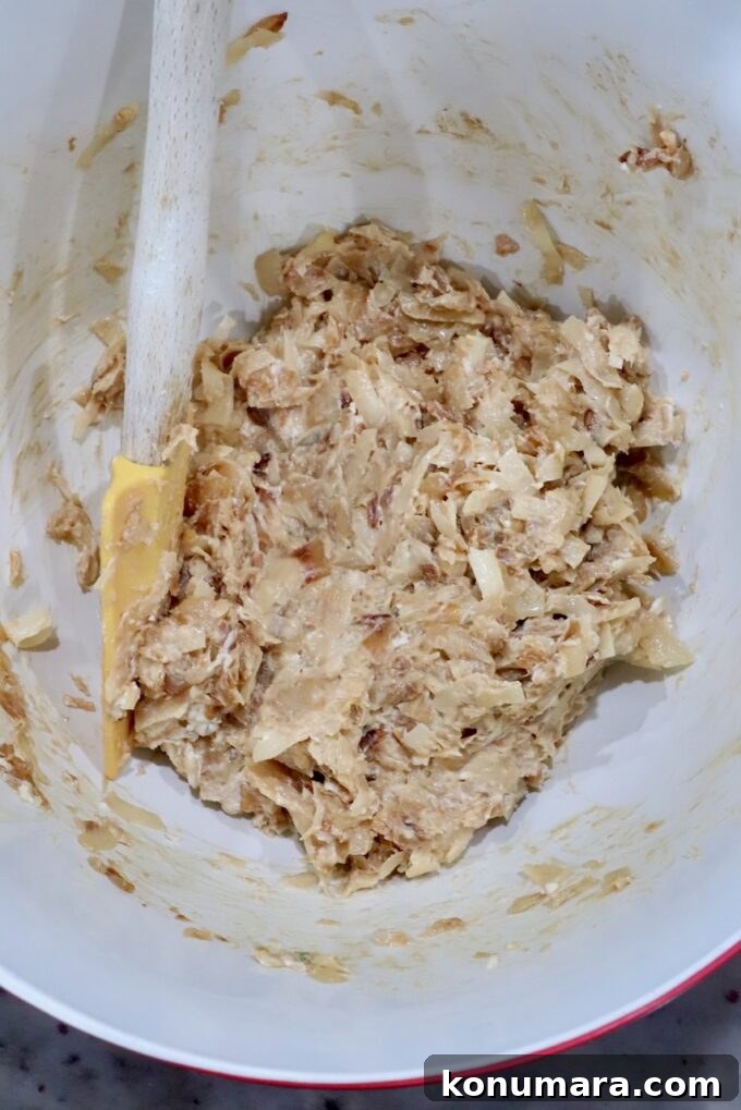 A mixing bowl contains a creamy caramelized onion mixture with a yellow spatula in the bowl.