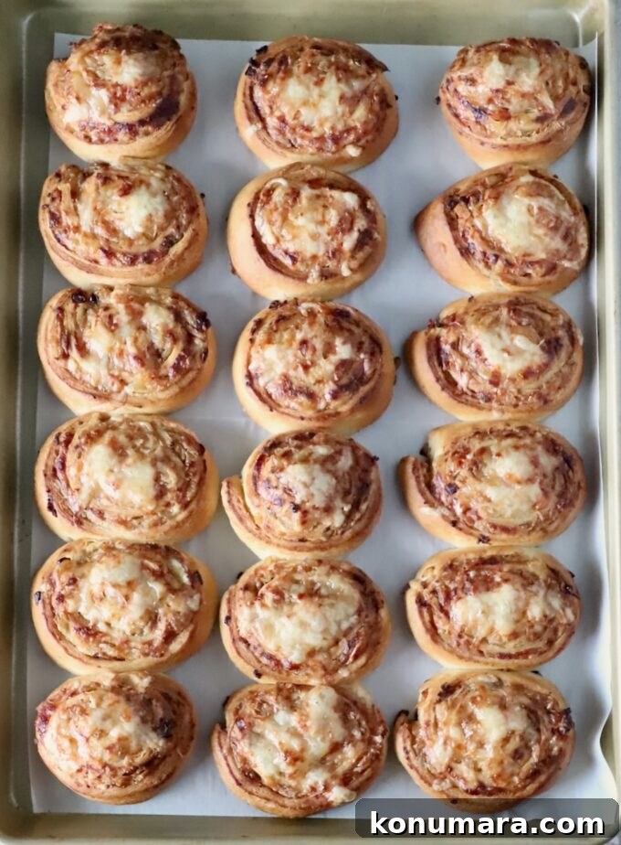 Eighteen golden-brown cheese and caramelized onion rolls on a baking sheet, evenly arranged in three rows.
