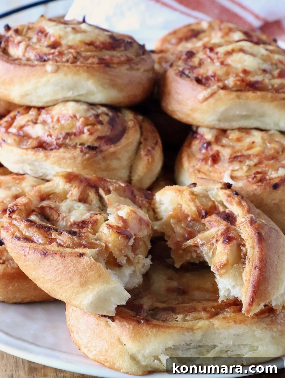 A plate of golden-brown, onion and cheese-filled pastries stacked up on a plate. The pastries have a flaky texture, with one torn open, revealing gooey, melted cheese inside.