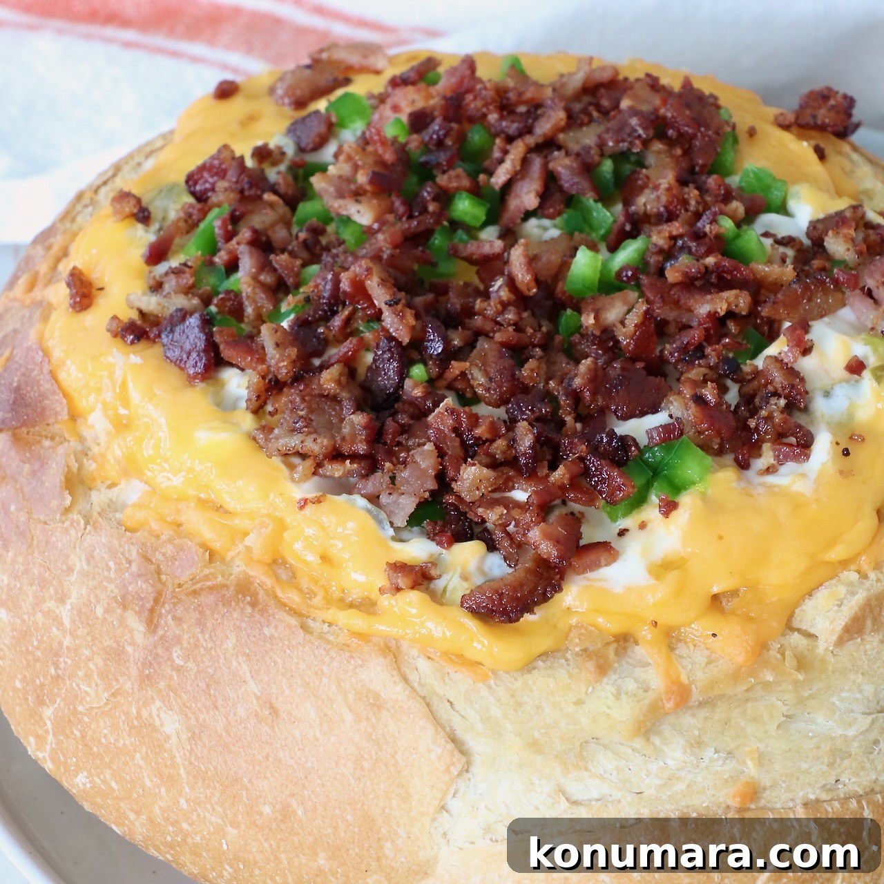Round bread loaf hollowed and filled with melted cheese, topped with crispy bacon bits and chopped green peppers