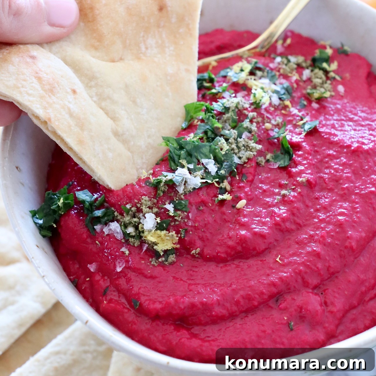 beet hummus in bowl with piece of pita bread dipped into the hummus