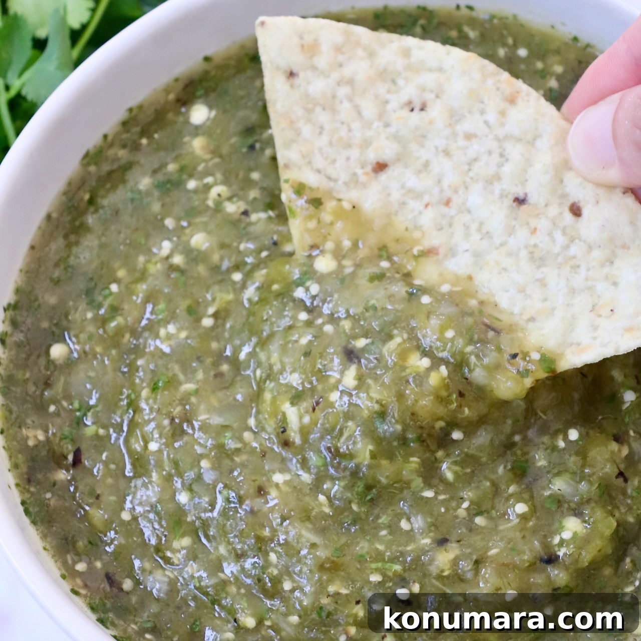tomatillo salsa in a bowl with a hand dipping a tortilla chip in the salsa