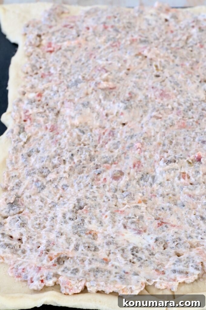 crescent roll dough covered in a cream cheese sausage mixture on a cutting board