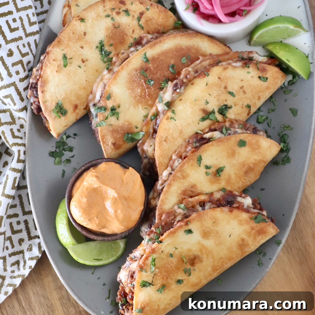 crispy tacos stacked up on a plate with lime wedges and a small bowl of chipotle sauce