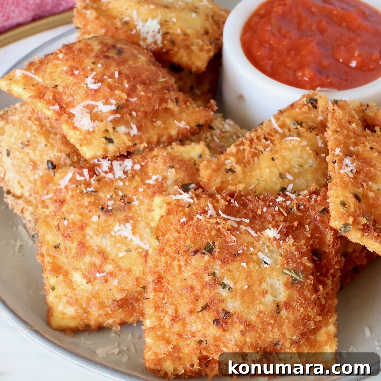 toasted raviolis stacked up on a plate with a small bowl of marinara sauce on the plate
