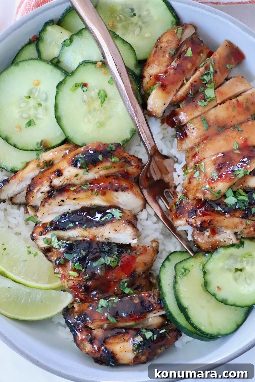 Authentic Thai Basil Chicken Stir-Fry (Pad Kra Pao) 2 Grilled, sliced chicken with glaze on rice, topped with herbs, served with cucumber slices, lime wedges, and a fork on a white plate.