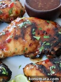 Grilled Thai glazed chicken thighs are topped with fresh herbs on a white plate. A small bowl of dipping sauce is visible on the side.