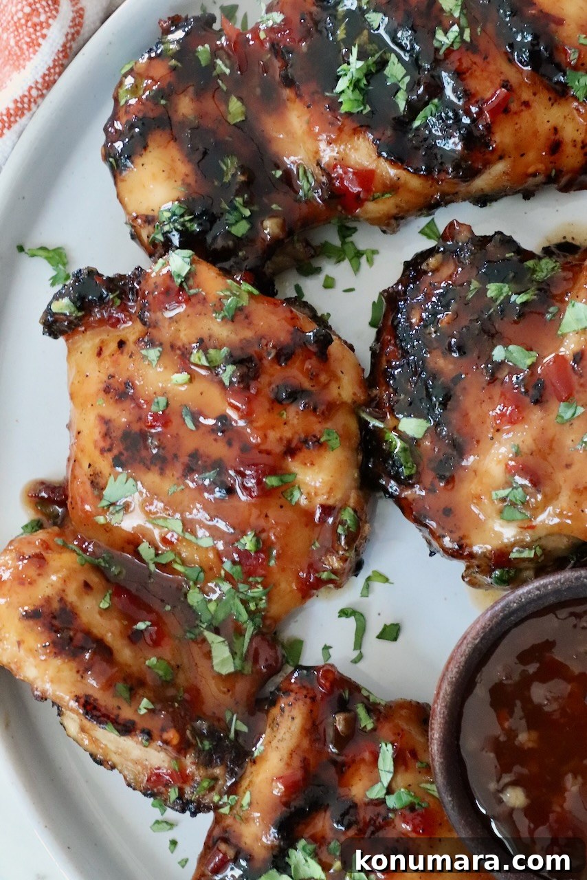 Authentic Thai Basil Chicken Stir-Fry (Pad Kra Pao) 8 Grilled glazed chicken thighs are topped with fresh herbs on a white plate. A small bowl of dipping sauce is visible on the side.