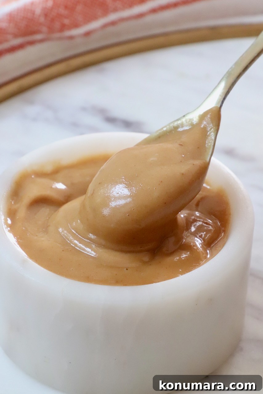Creamy Thai Peanut Dressing for Salads and Bowls 2 A spoon dips into creamy peanut butter dressing in a small white bowl on a marble surface.
