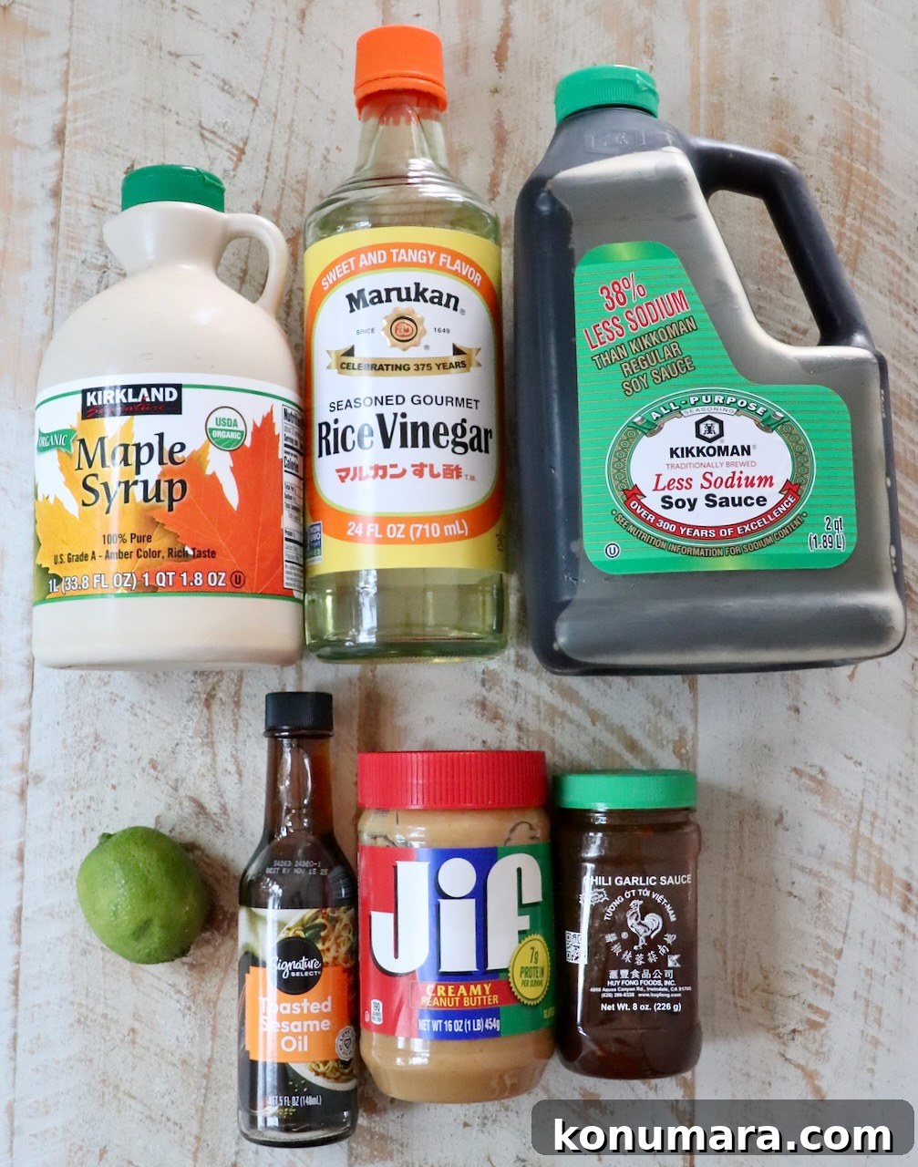 Creamy Thai Peanut Dressing for Salads and Bowls 3 Assorted food items on a rustic table: maple syrup, rice vinegar, soy sauce, sesame oil, peanut butter, chili garlic sauce, and a lime.