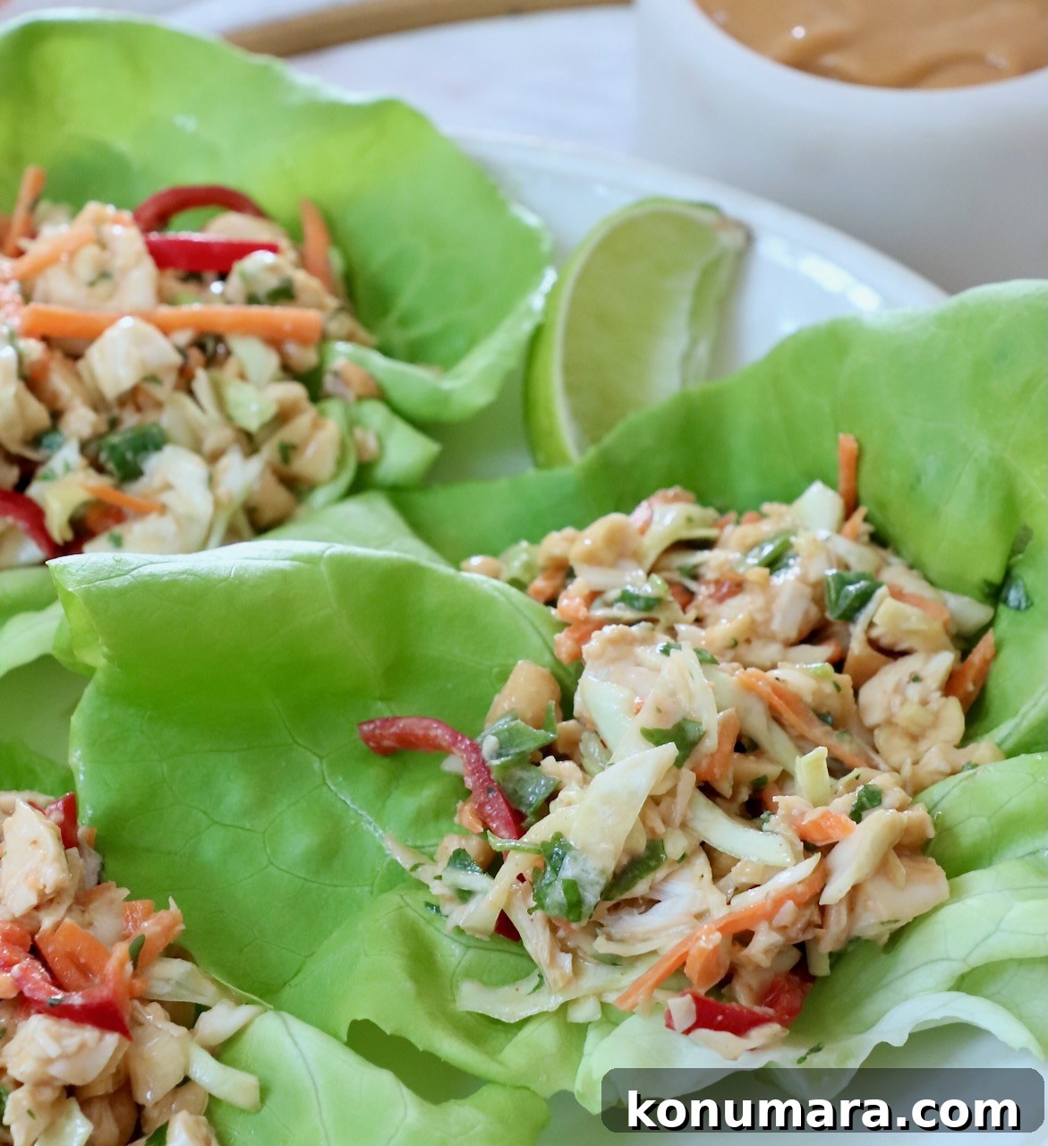 Fresh lettuce wraps filled with chopped chicken, carrots, and red peppers. A lime wedge and creamy dip are visible in the background.