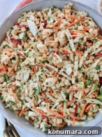 A vibrant Thai chicken salad in a bowl with shredded cabbage, carrots, peanuts, and cilantro. Two lime wedges are on top, and a creamy dressing is on the side.