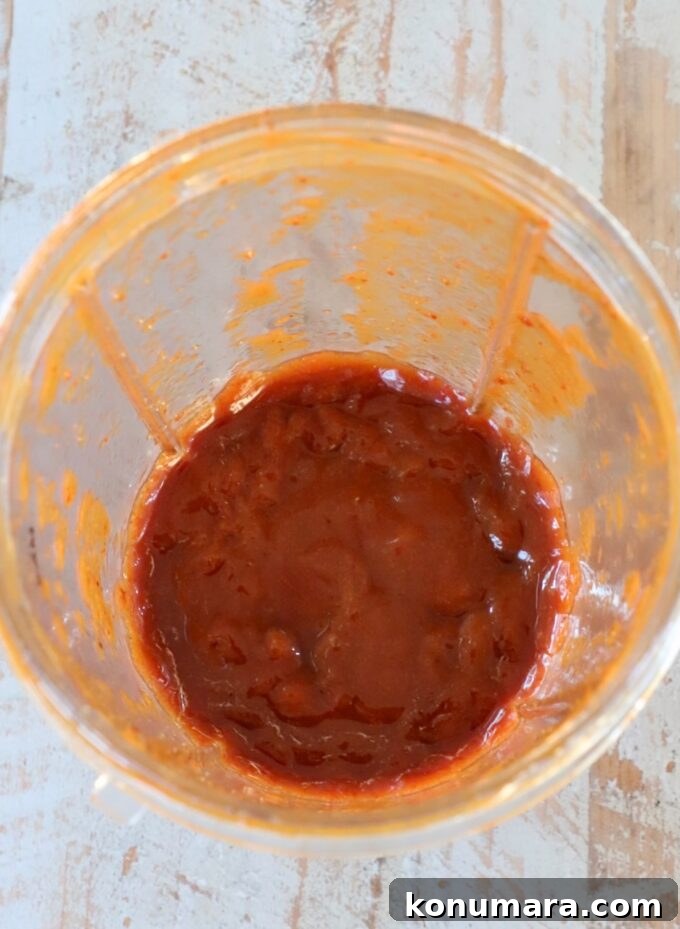 Chipotle Honey Glazed Little Smokies 4 A blender cup partially filled with a smooth, red-orange chipotle sauce, sits on a wooden surface.