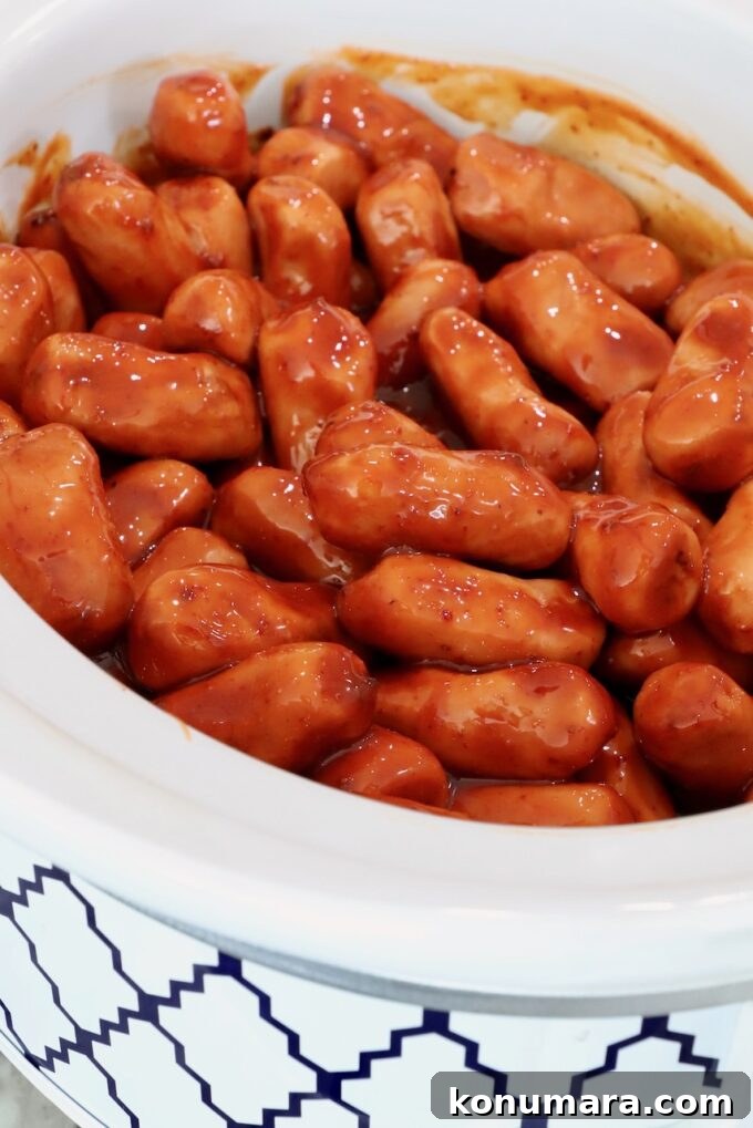 Chipotle Honey Glazed Little Smokies 5 A white crockpot filled with small sausages in a rich, glossy chipotle honey sauce.