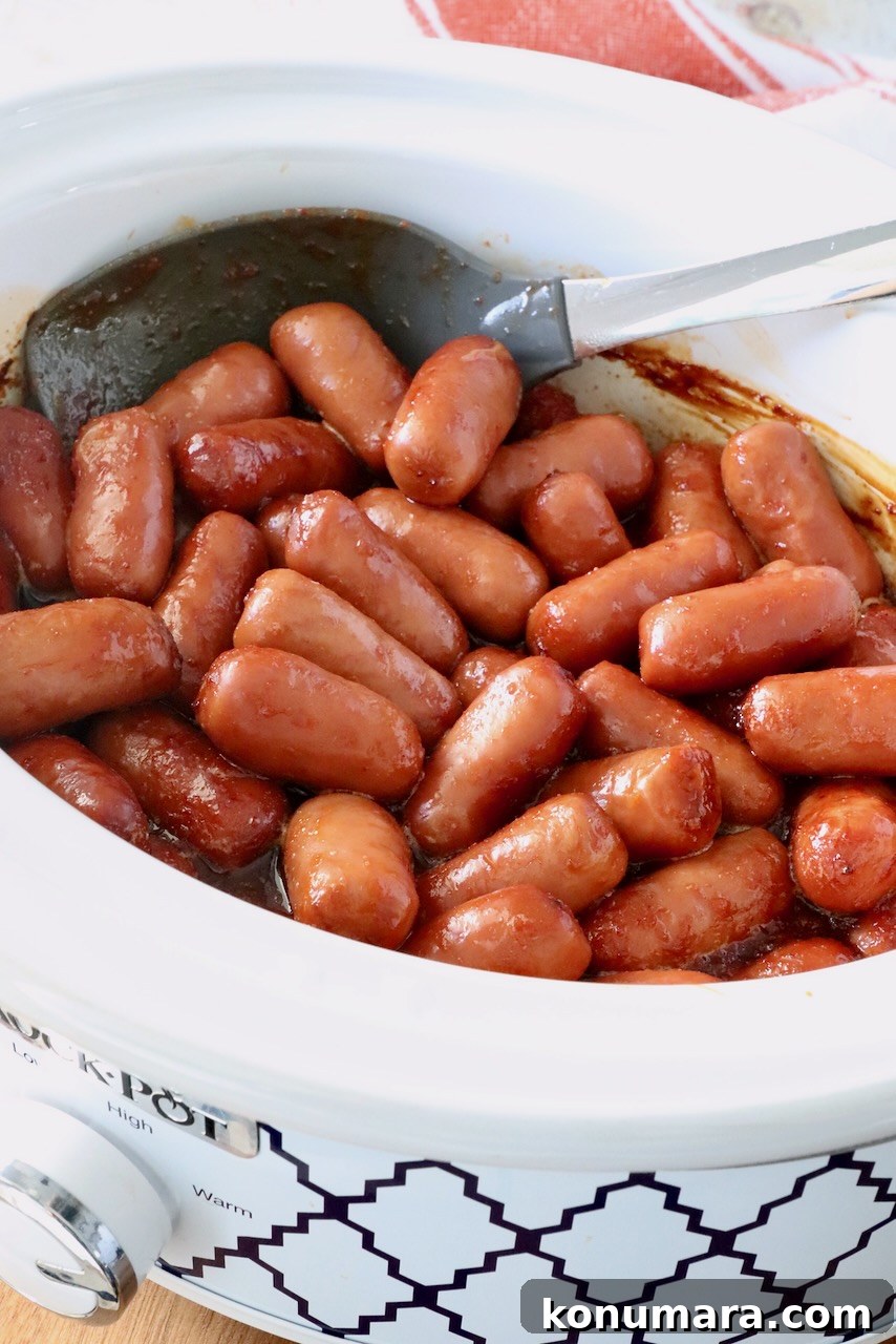 Chipotle Honey Glazed Little Smokies 6 Slow cooker filled with glossy cocktail sausages in a chipotle sauce, with a serving spoon resting inside.