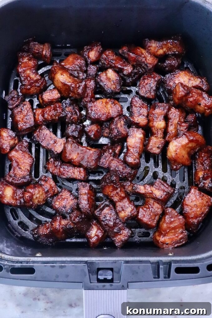 Crispy, golden-brown pork belly pieces in an air fryer basket, showing a rich glaze and succulent texture.