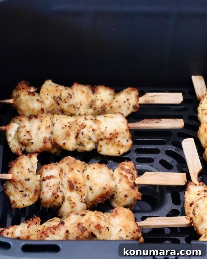 Cooked golden brown chicken skewers seasoned with herbs placed in an air fryer basket.
