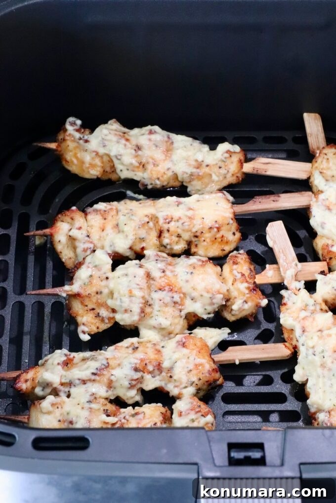 Cooked chicken skewers topped with creamy sauce in an air fryer basket.