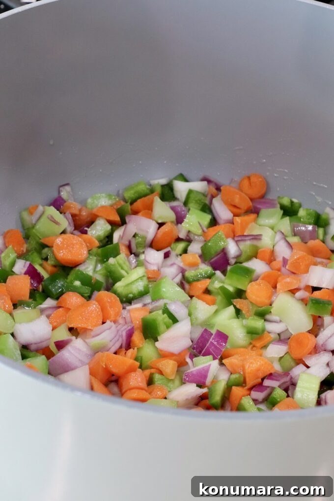 Chopped vegetables, including carrots, green peppers, onions, and celery, in a large gray pot