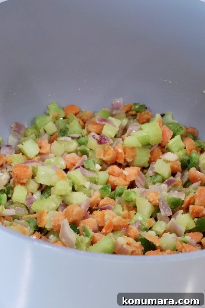 Chopped vegetables, including carrots, jalapeno peppers, onions, and celery, in a large gray pot, covered in flour