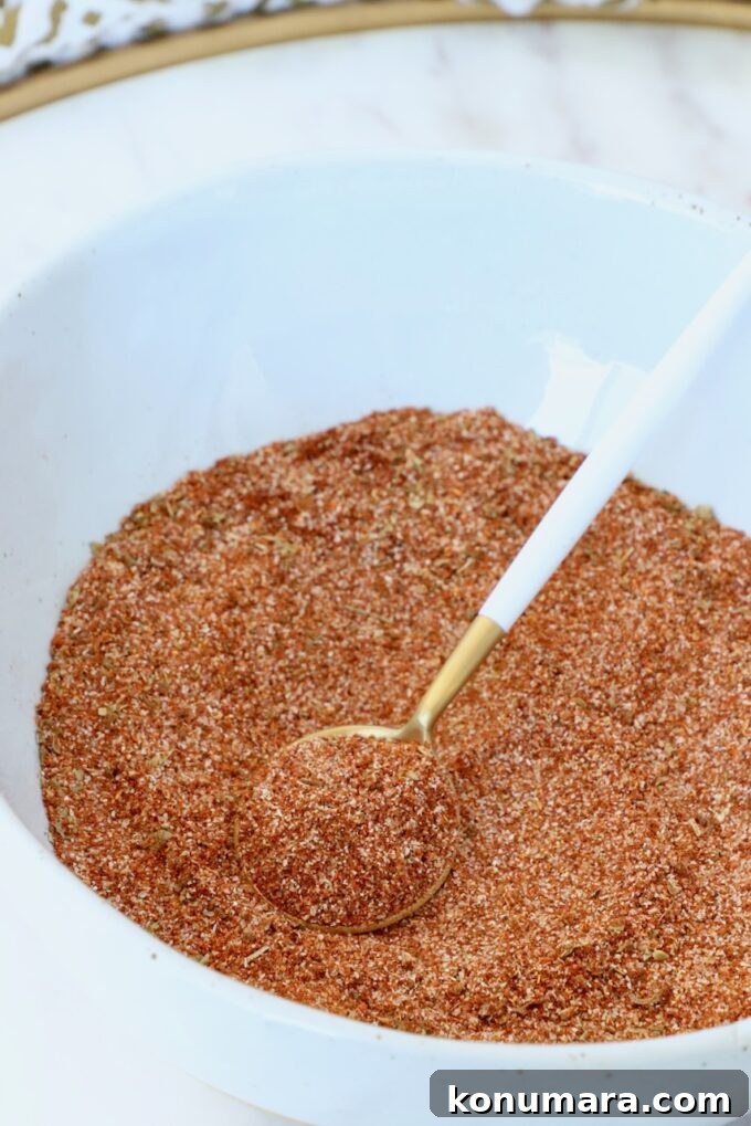 Close-up of a white bowl filled with reddish-brown spice mix. A gold and white spoon rests on top.