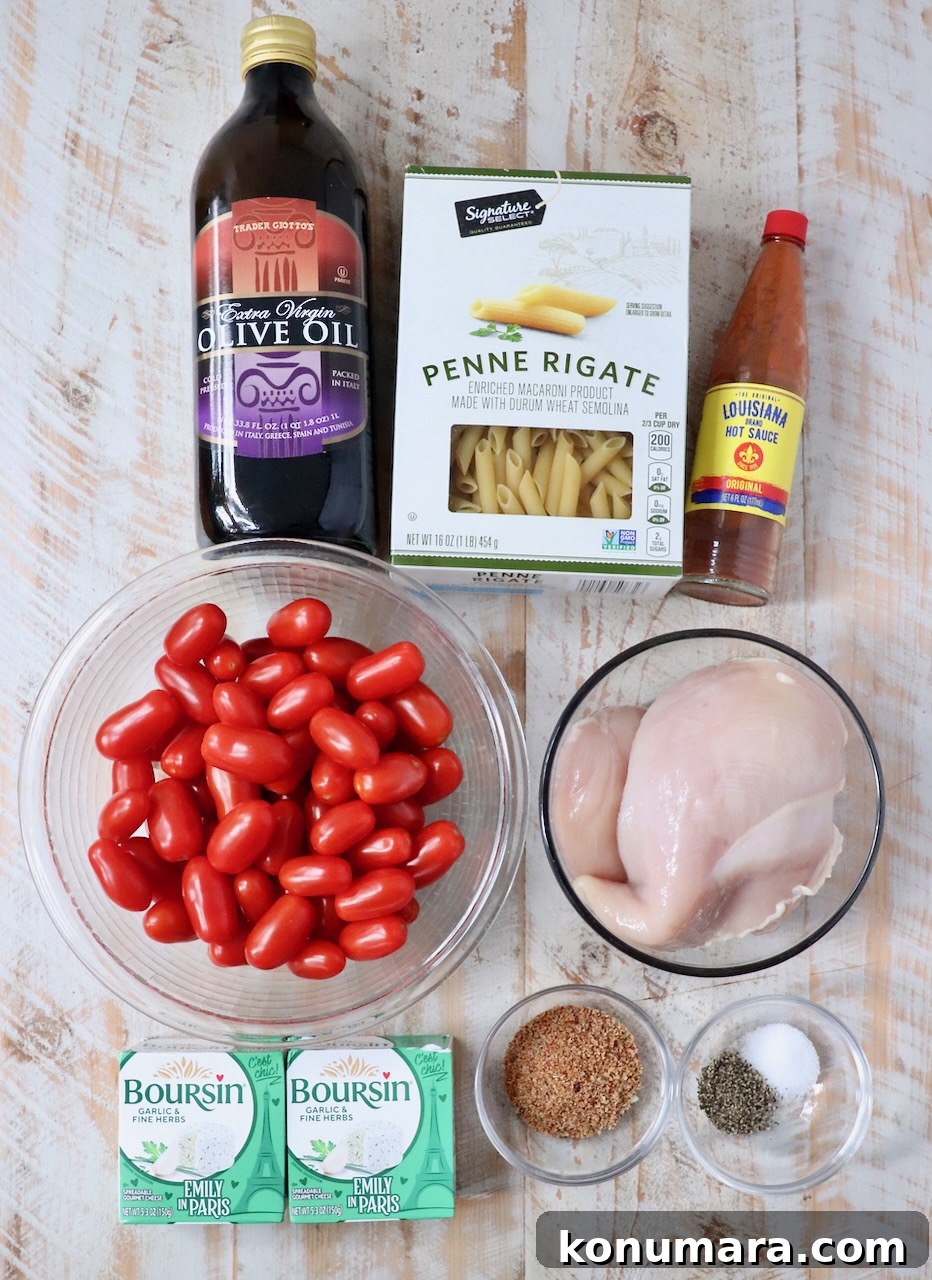 Ingredients for a pasta dish arranged on a wooden surface. Includes olive oil, penne pasta, hot sauce, cherry tomatoes, chicken breast, Boursin cheese, and seasoning.