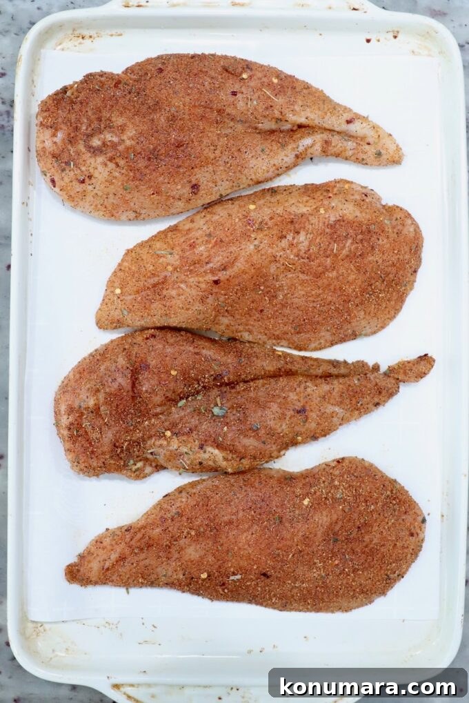 seasoned raw chicken breasts on a white baking sheet