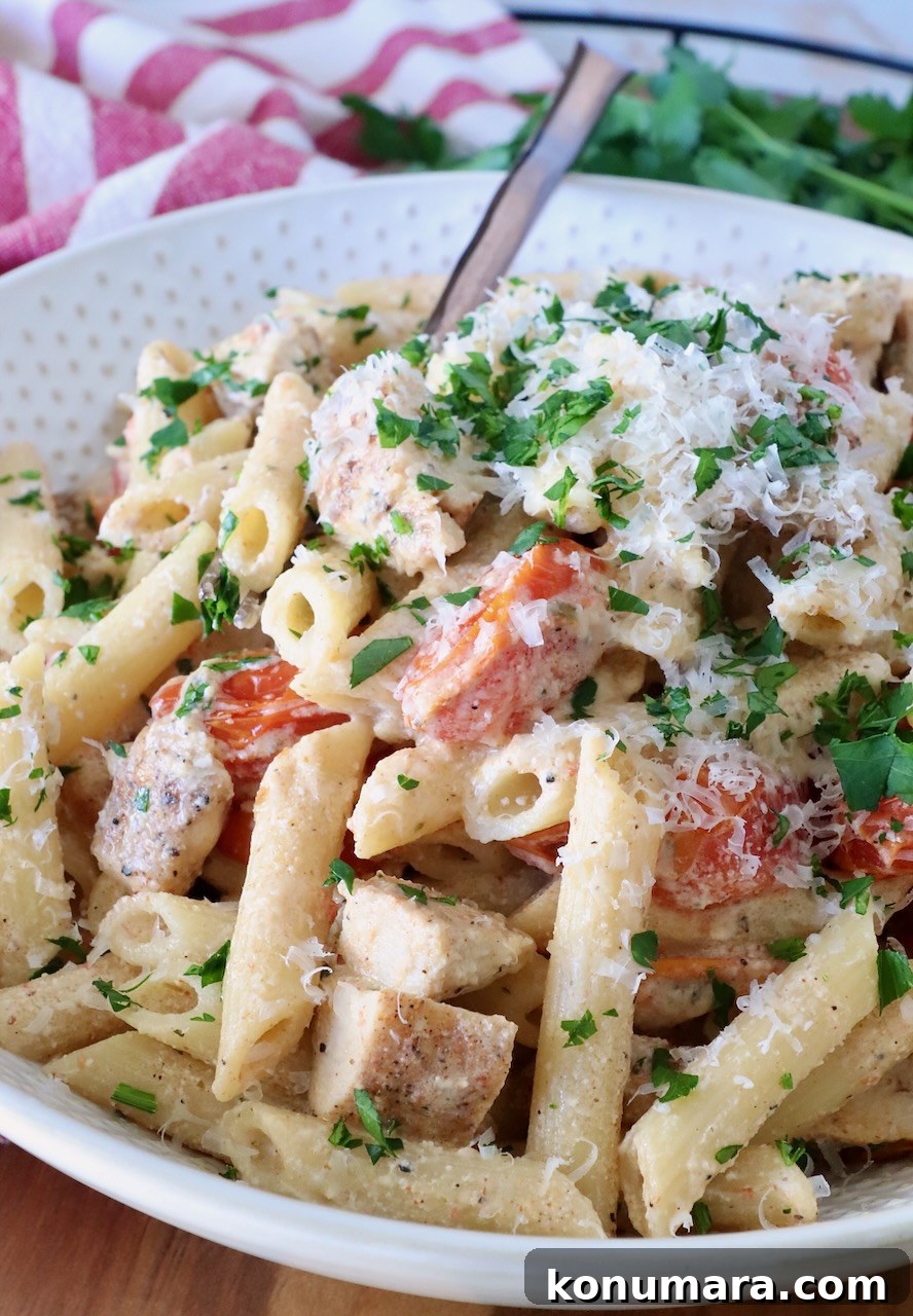 A creamy pasta dish with penne, diced chicken, cherry tomatoes, and parsley, topped with grated cheese.