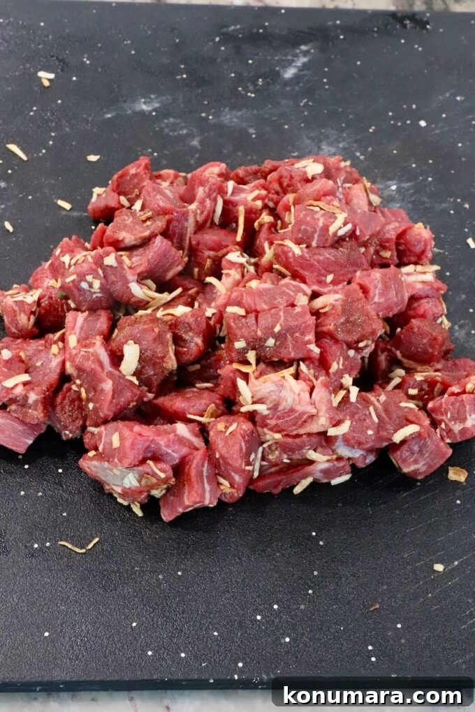 cubes of beef tossed with french onion seasoning on a black cutting board