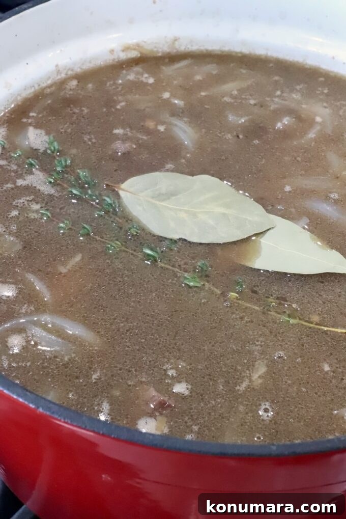 beef stew in a pot topped with bay leaves and thyme sprigs