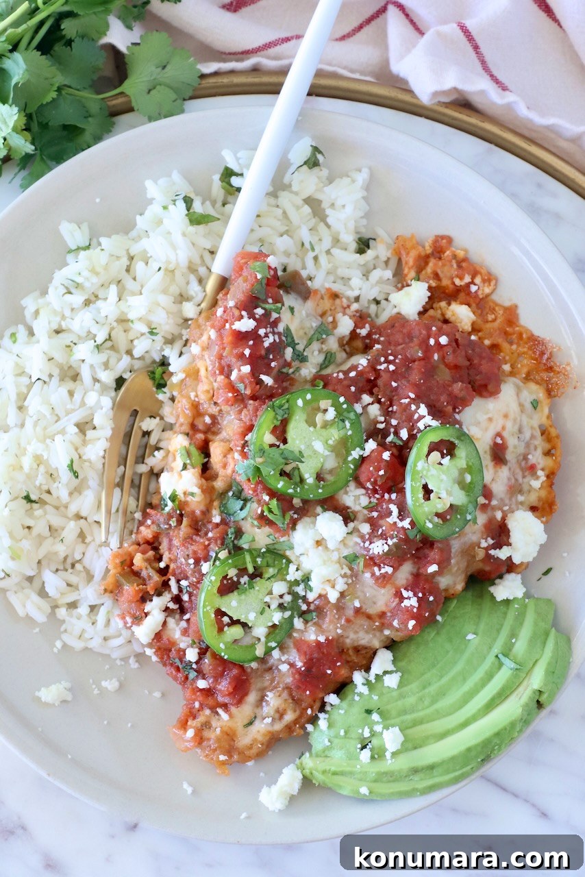 Crispy Mexican-Style Chicken Parmesan with Chipotle Sauce 2 A plate of Mexican chicken parmesan topped with salsa, jalapeño slices, and cheese, served with cilantro rice and avocado slices on the side.