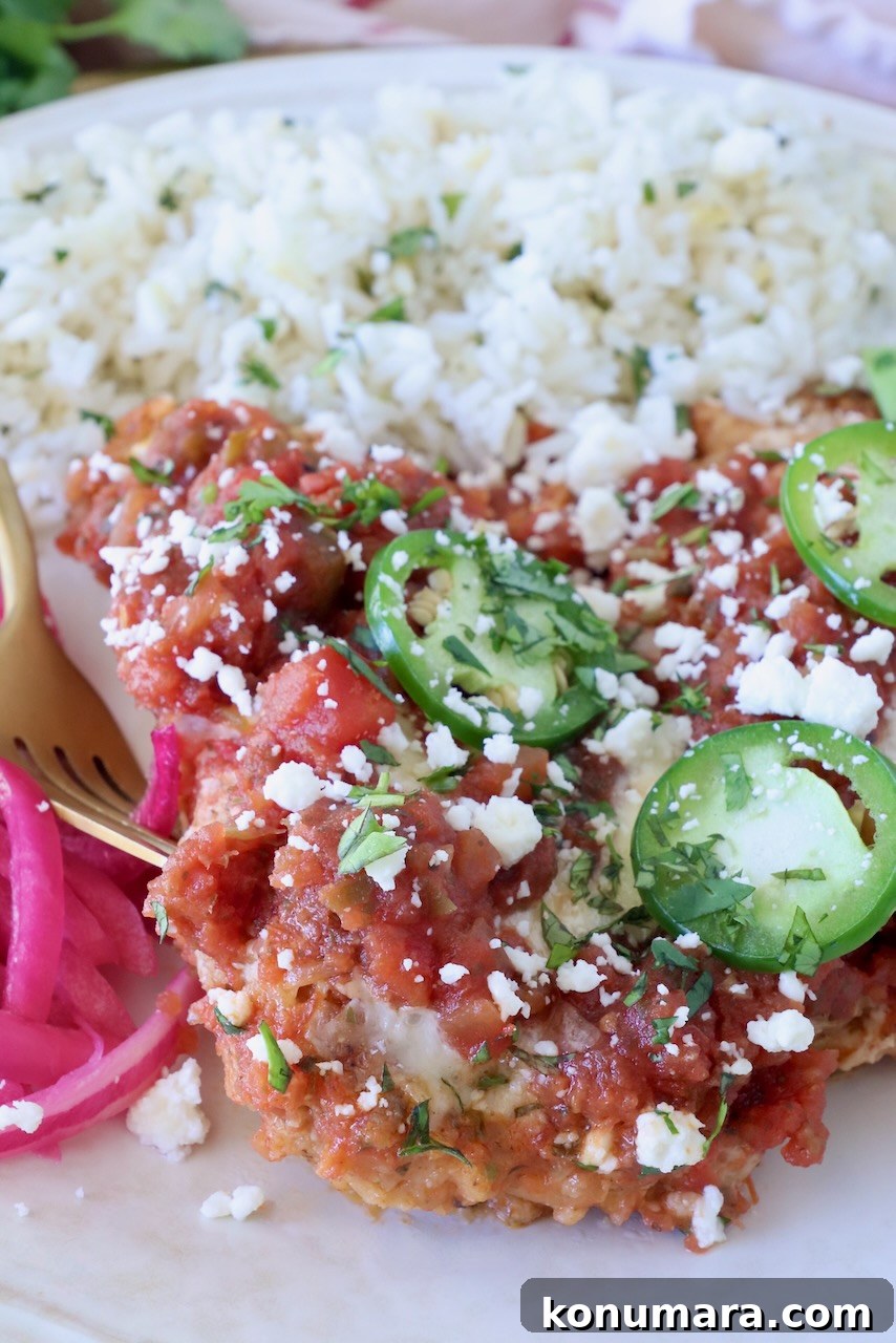 Crispy Mexican-Style Chicken Parmesan with Chipotle Sauce 6 A plate with rice and Mexican chicken parmesan, topped with sliced jalapeños and crumbled cheese, garnished with cilantro and a side of pickled onions