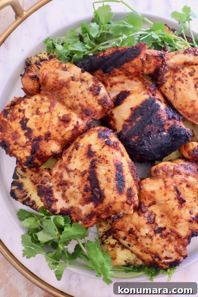Grilled chicken thighs with a smoky char, arranged on a white plate. Served with fresh cilantro on the side.