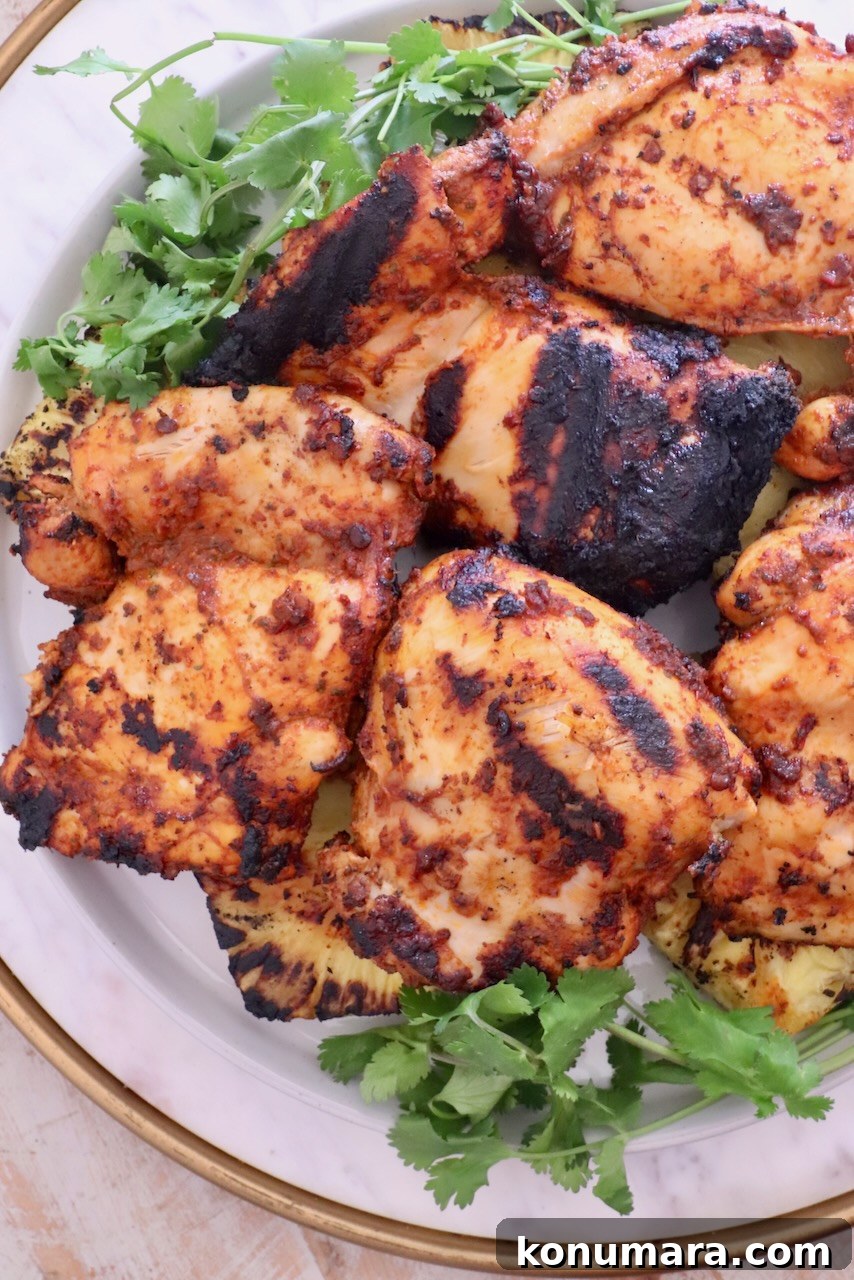 How to Make Chicken Al Pastor Tacos with Pineapple 2 Grilled chicken thighs with charred marks on a white plate, garnished with fresh cilantro.