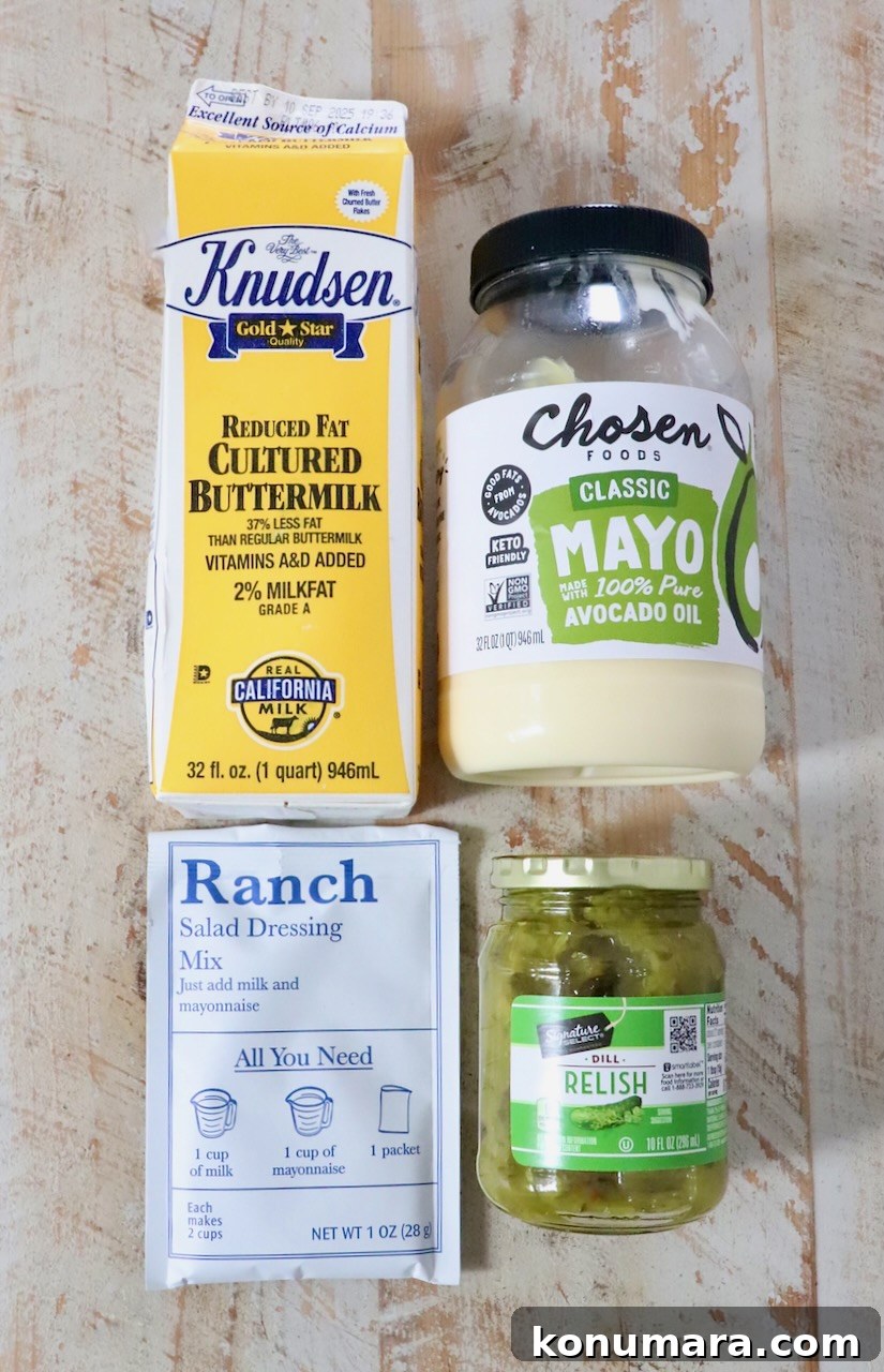 Creamy Dill Pickle Ranch Dressing Recipe 3 Four food items on a wooden surface: buttermilk carton, avocado oil mayo jar, ranch dressing mix packet, and dill relish jar.