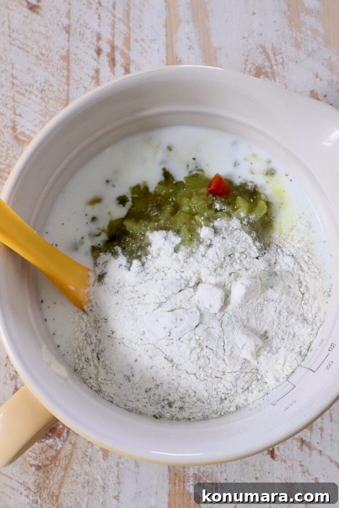 Creamy Dill Pickle Ranch Dressing Recipe 4 Mixing bowl with ranch dressing mix, buttermilk, and dill pickle relish. A yellow spatula rests in the bowl on a wooden surface.