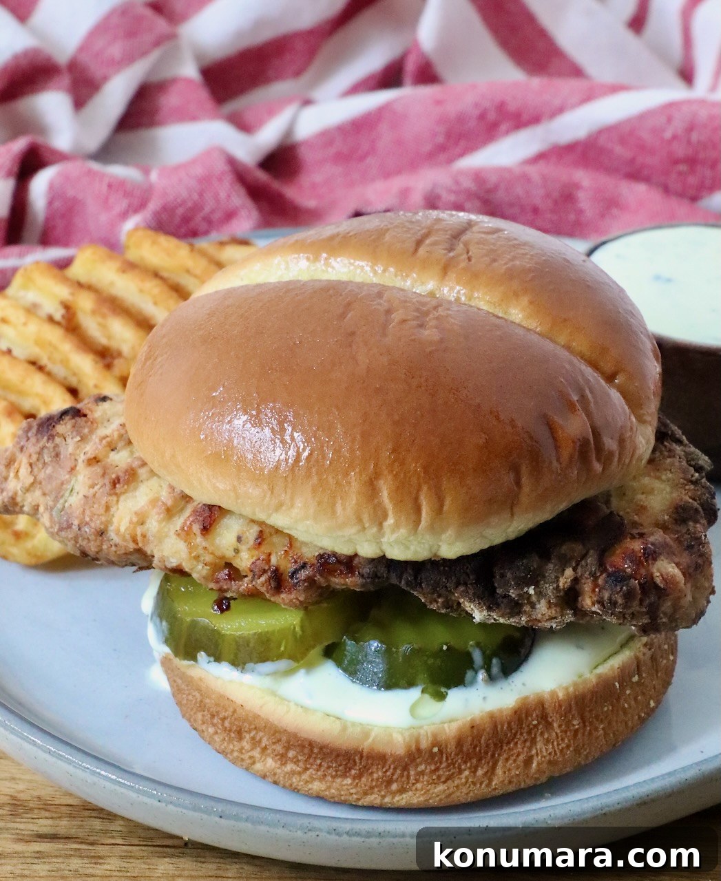 Crispy Air Fryer Chicken Sandwich Recipe 13 A crispy air fried chicken sandwich on a soft bun with pickles and creamy sauce, served with waffle fries on a plate.