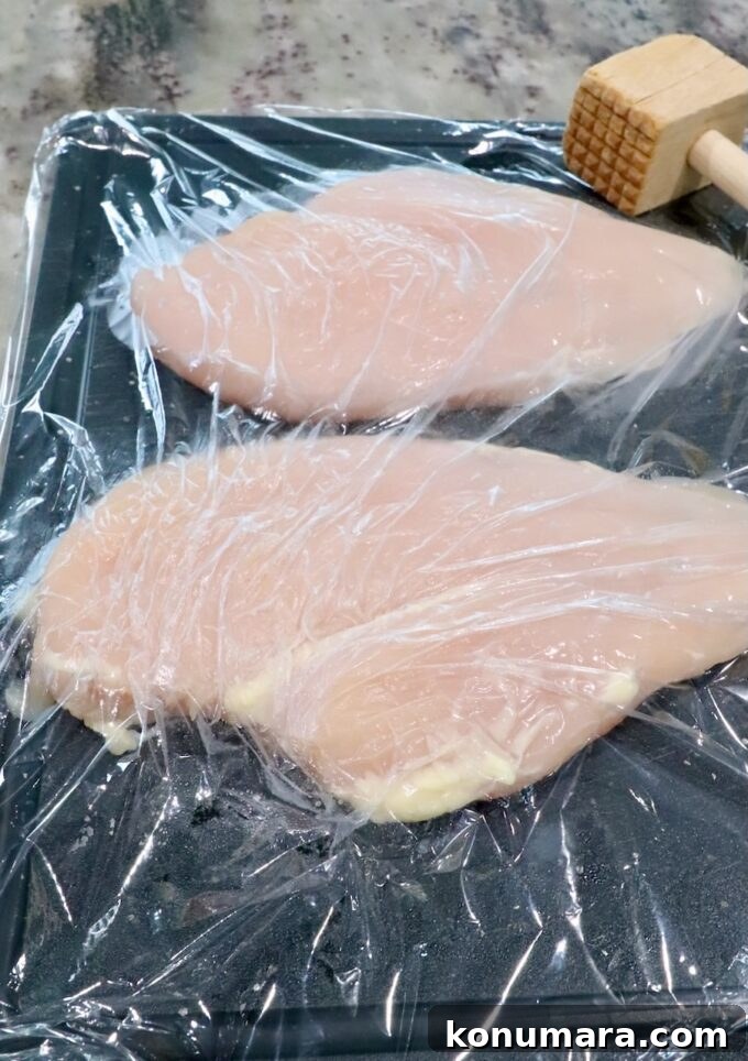 Crispy Air Fryer Chicken Sandwich Recipe 4 chicken breasts on a cutting board under a piece of plastic wrap