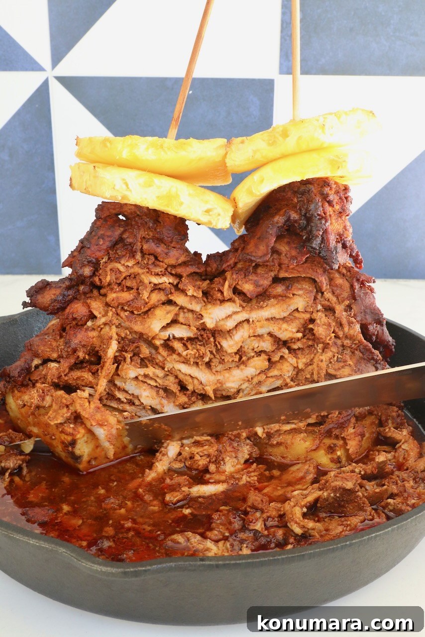 Slow-Roasted Al Pastor Pork Tacos 2 A stack of marinated, cooked pork layered on skewers, topped with pineapple slices, in a cast iron skillet. A knife slices through the juicy, cooked meat.