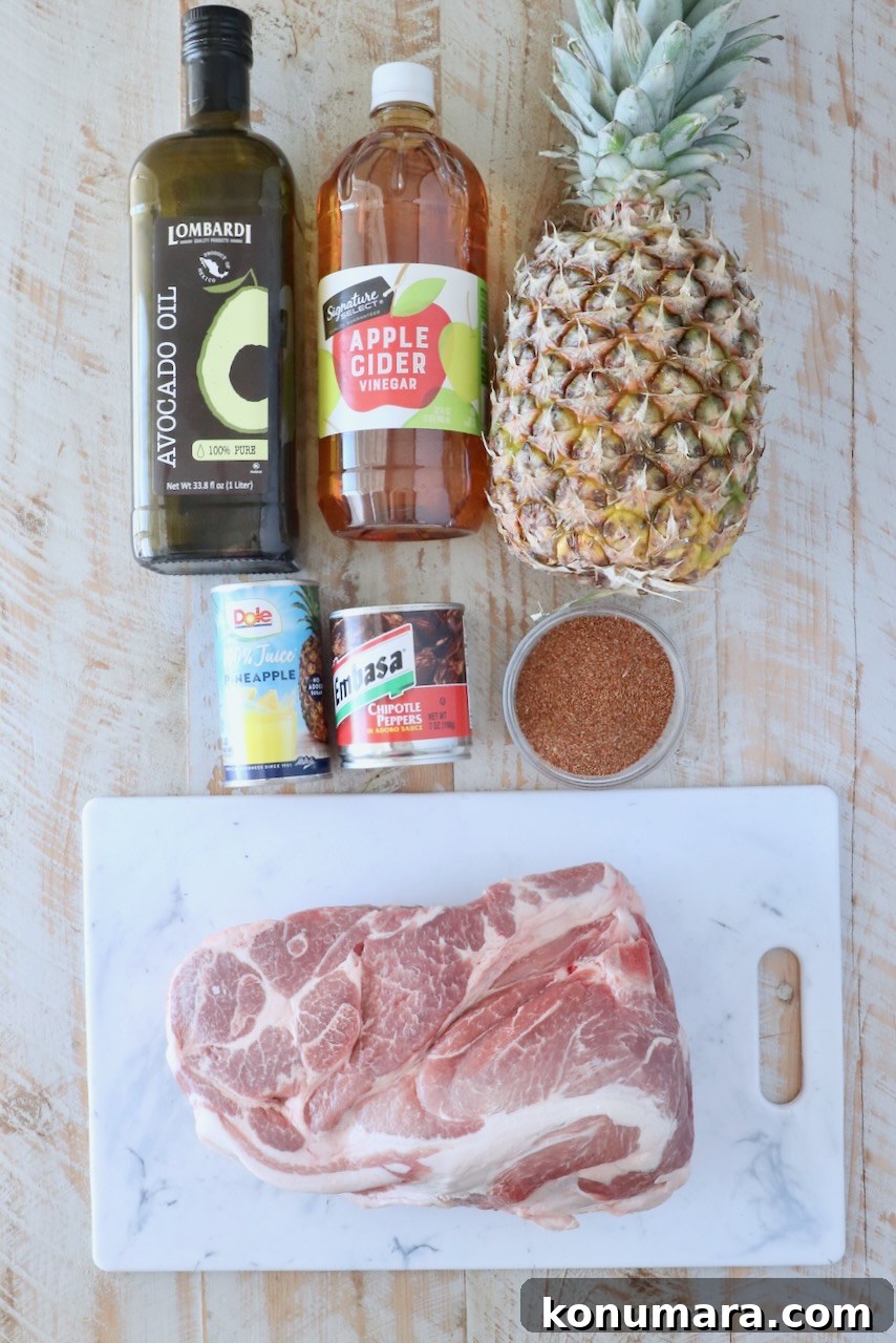 Slow-Roasted Al Pastor Pork Tacos 3 Ingredients for al pastor are arranged on a wooden surface. Items include avocado oil, apple cider vinegar, a whole pineapple, canned pineapple juice, chipotle peppers, a bowl of spices, and a raw pork shoulder on a marble board.