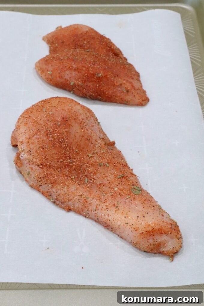 Seasoned chicken breasts on a parchment-lined baking sheet