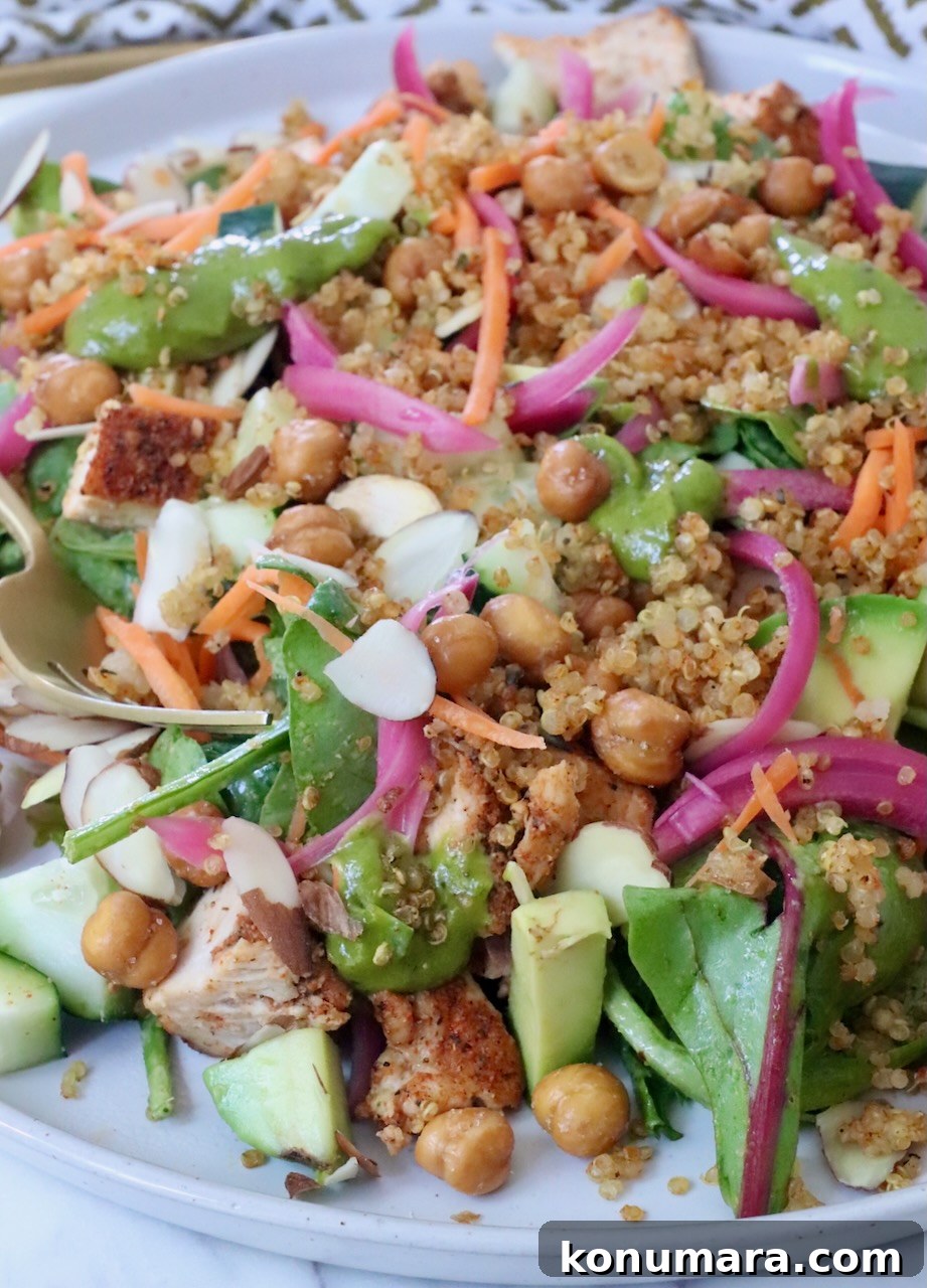 A vibrant salad with greens, quinoa, chickpeas, sliced almonds, carrots, and pickled onions on a plate.