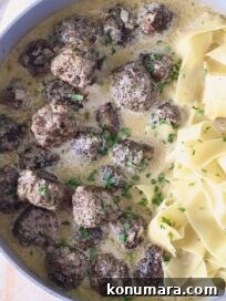 meatballs au poivre in a skillet with cooked egg noodles