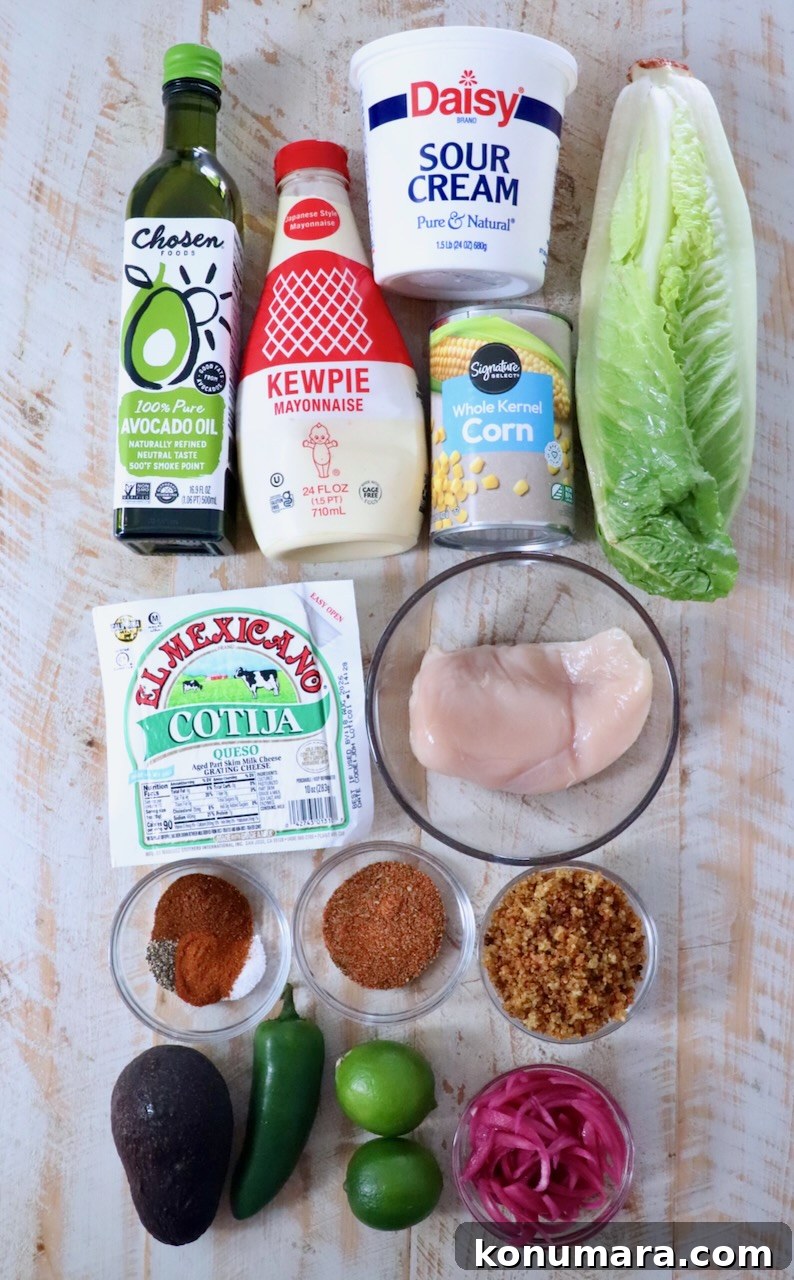 Mexican Street Corn Chicken Bowls Recipe with Cotija and Lime 3 Ingredients laid out: avocado oil, sour cream, mayonnaise, corn, lettuce, chicken breast, cotija cheese, spices, avocado, jalapeño, limes, and pickled onions.