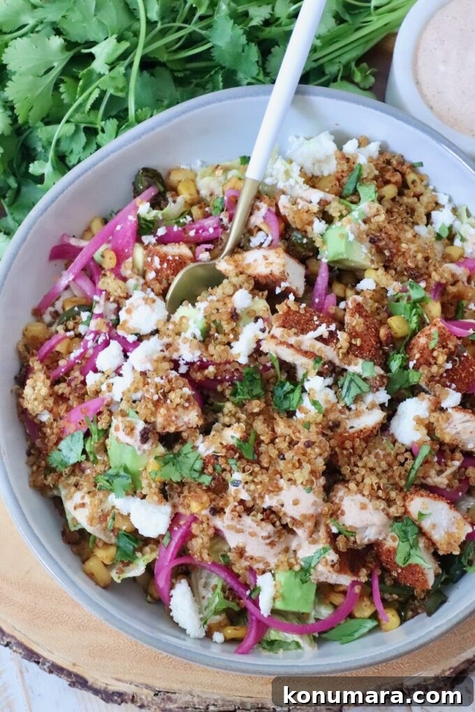 How to Make Crispy Quinoa 7 A vibrant salad in a bowl featuring quinoa, grilled chicken, avocado, corn, pickled onions, and crumbled cheese. Fresh cilantro and dressing are next to it.