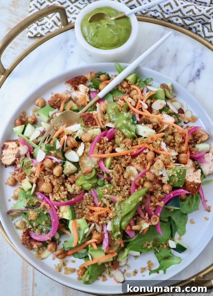 How to Make Crispy Quinoa 8 A vibrant salad with greens, quinoa, chickpeas, sliced almonds, carrots, and pickled onions on a platter. A cup of green dressing is beside it.