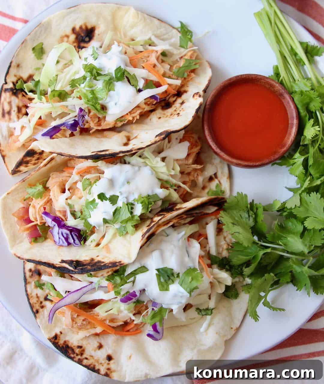 Three buffalo chicken tacos on white plate with side small bowl of buffalo sauce