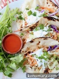 Tacos on plate with small wooden bowl of buffalo sauce on the side