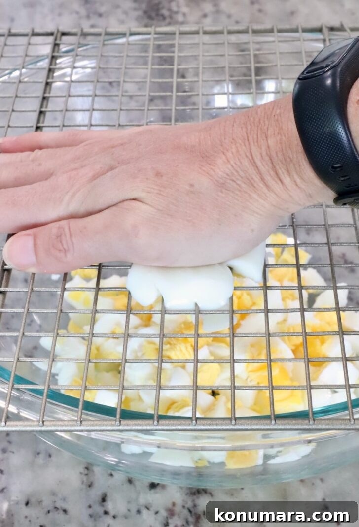 Spicy Miso Egg Salad with Chili Crisp Recipe 6 A hand presses a hard-boiled egg through a metal cooling rack, dicing it into a bowl below.