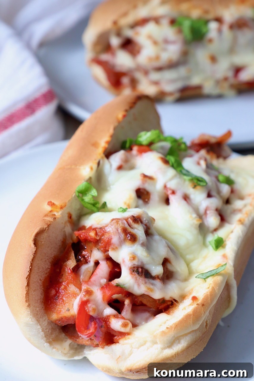 Classic Italian Sausage and Peppers Recipe 6 sausage and peppers in sub sandwich topped with melted mozzarella cheese on white plate